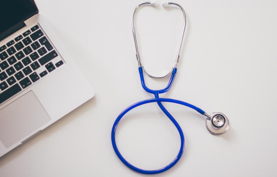 A stethoscope next to a laptop on a clinic desk